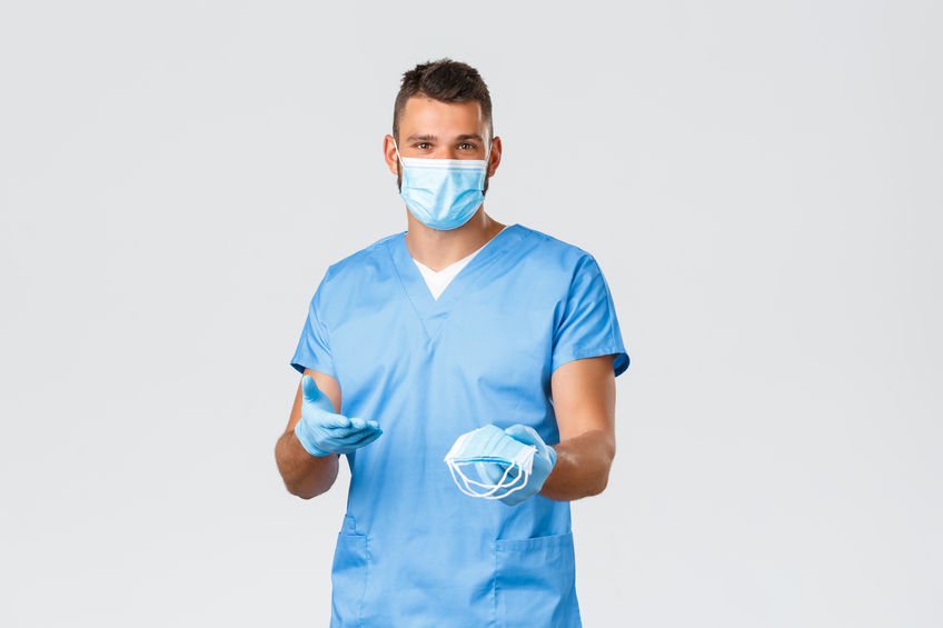 A man in blue scrubs reaches out with PPE masks